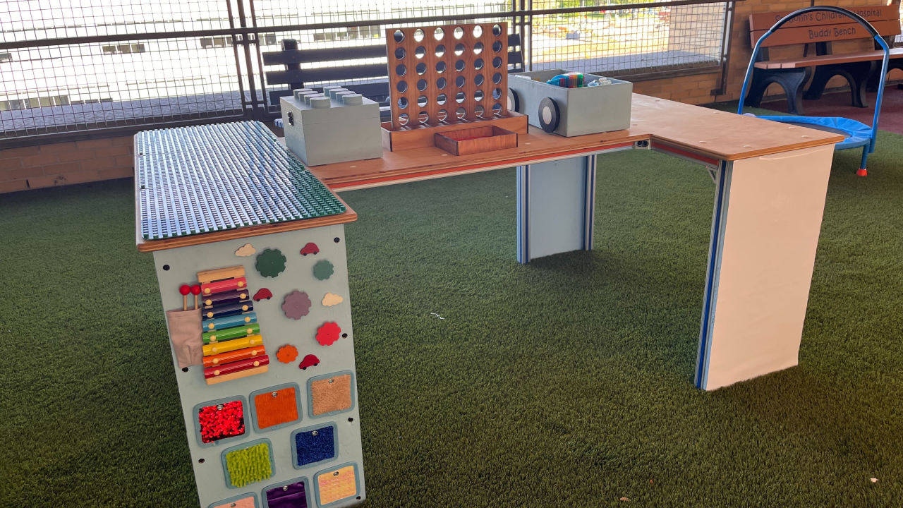 A block-I shaped table consisting of a wooden top, aluminium frame and activities on side panels